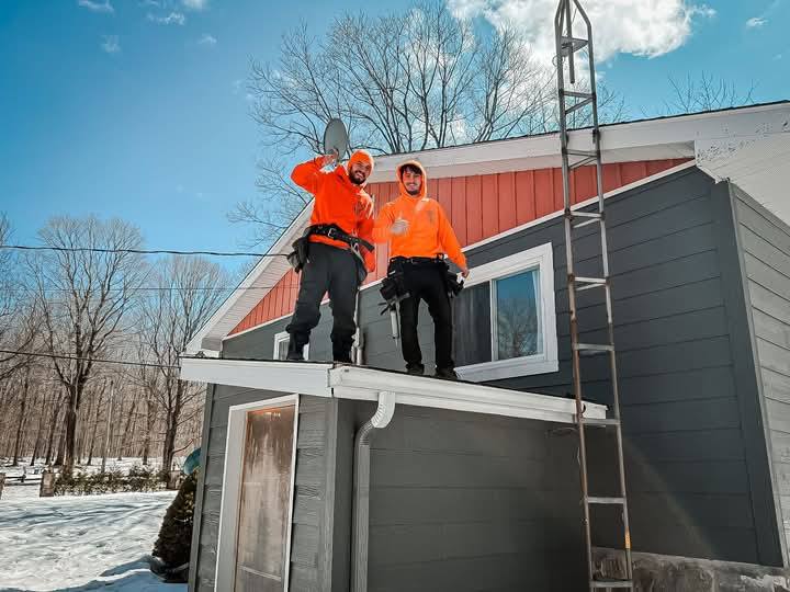 Two technicians in orange on a Montreal roof